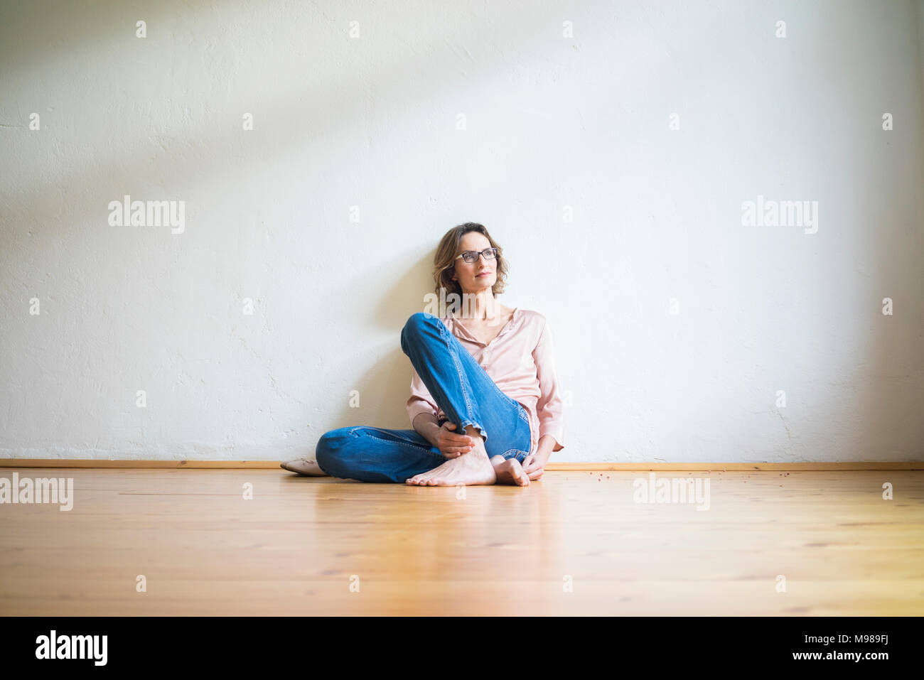 Donna matura seduta sul pavimento nella stanza vuota pensando Foto Stock