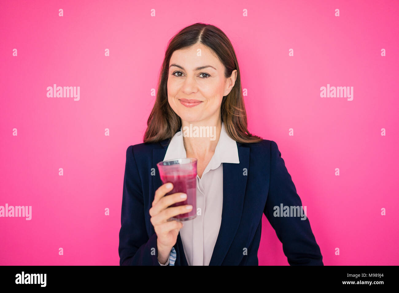 Ritratto di sorridere imprenditrice nella parte anteriore della parete rosa azienda bicchiere di succo di frutta Foto Stock