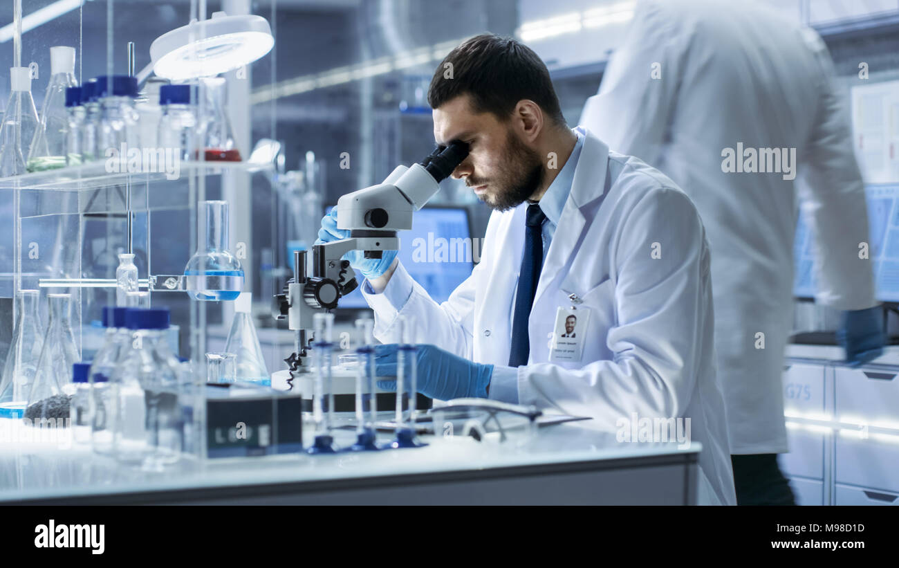 Research Scientist guarda nel microscopio al centro di ricerca. Egli la conduce esperimenti in laboratorio moderno. Foto Stock