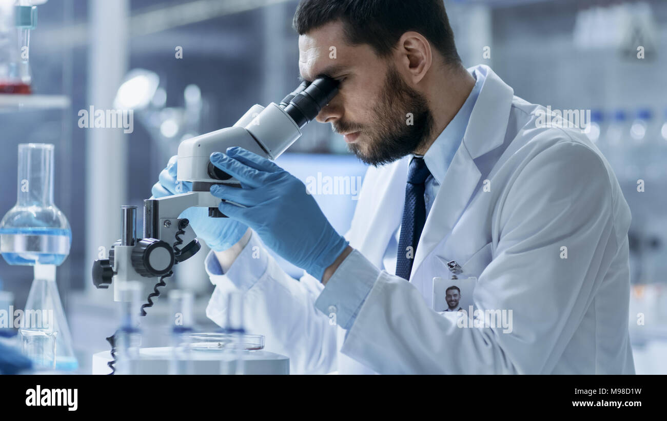 Research Scientist guarda nel microscopio. Egli la conduce esperimenti in laboratorio moderno. Foto Stock