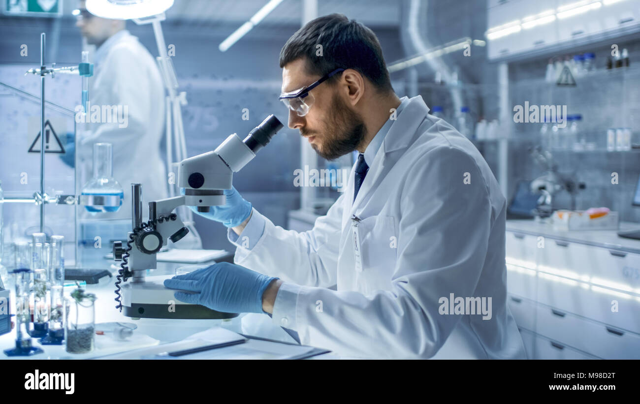 In un moderno laboratorio scienziato conduce esperimenti con materiali organici. Lui sta cercando in un microscopio. Foto Stock