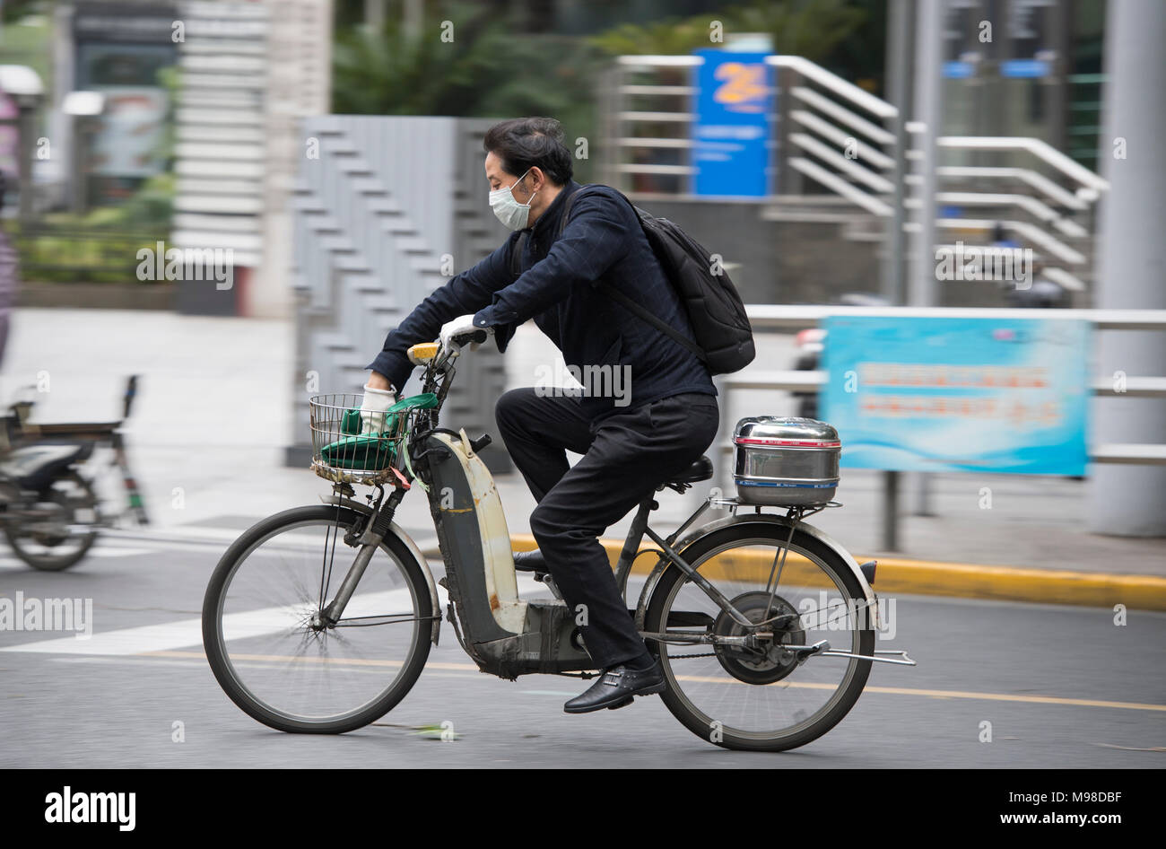 Uomo che indossa una maschera facciale a cavallo di uno scooter a Shanghai in Cina Foto Stock