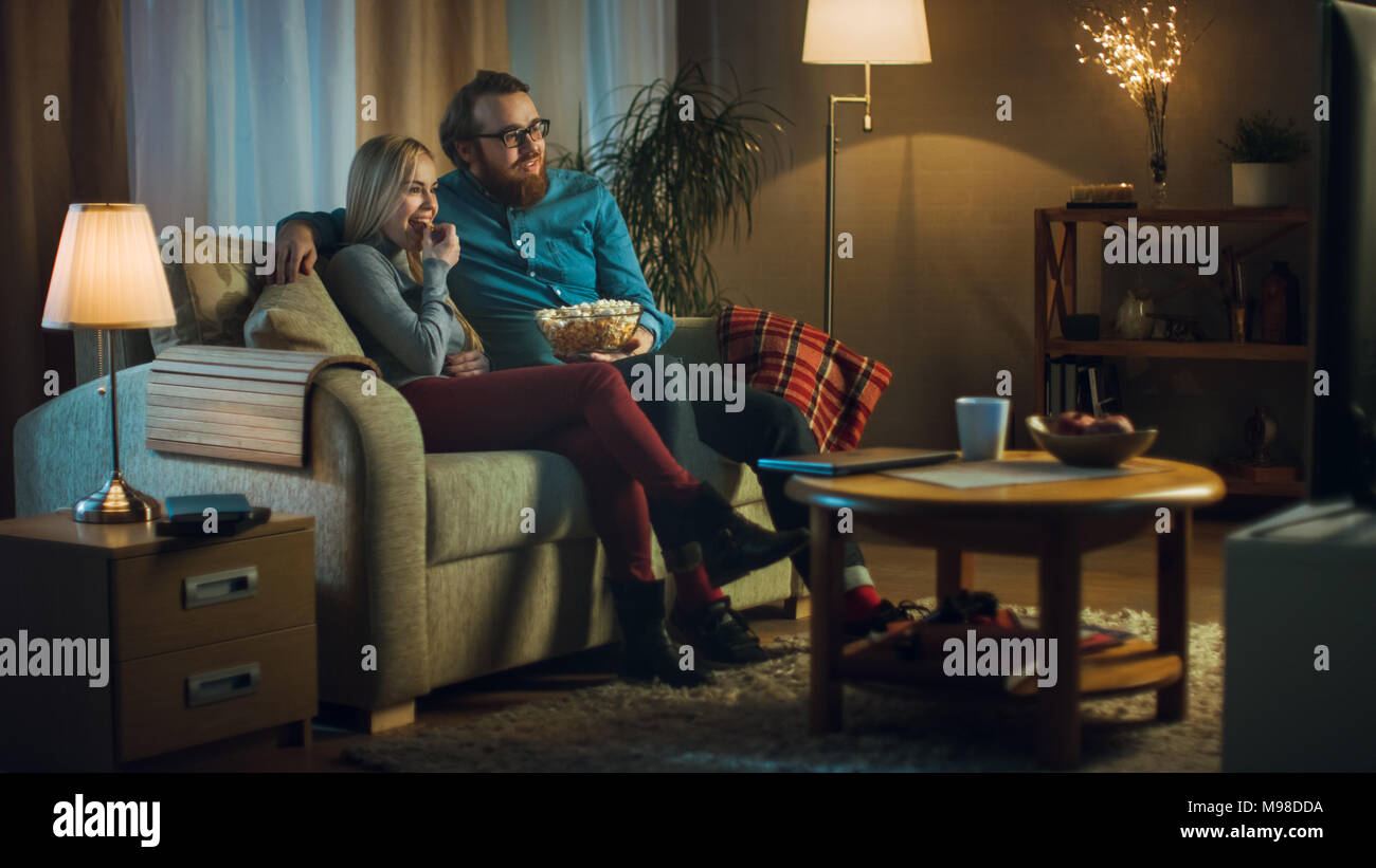 In serata l uomo e la donna sono seduti sul divano a guardare la TV e mangiare popcorn. Soggiorno è accogliente. Foto Stock