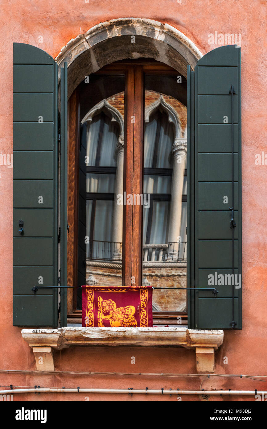 Stilted Gothic lancet arcate di epoca bizantina e influenza moresca con colonne si riflette in una stilted arch finestra aperta con persiane verdi e flag Foto Stock