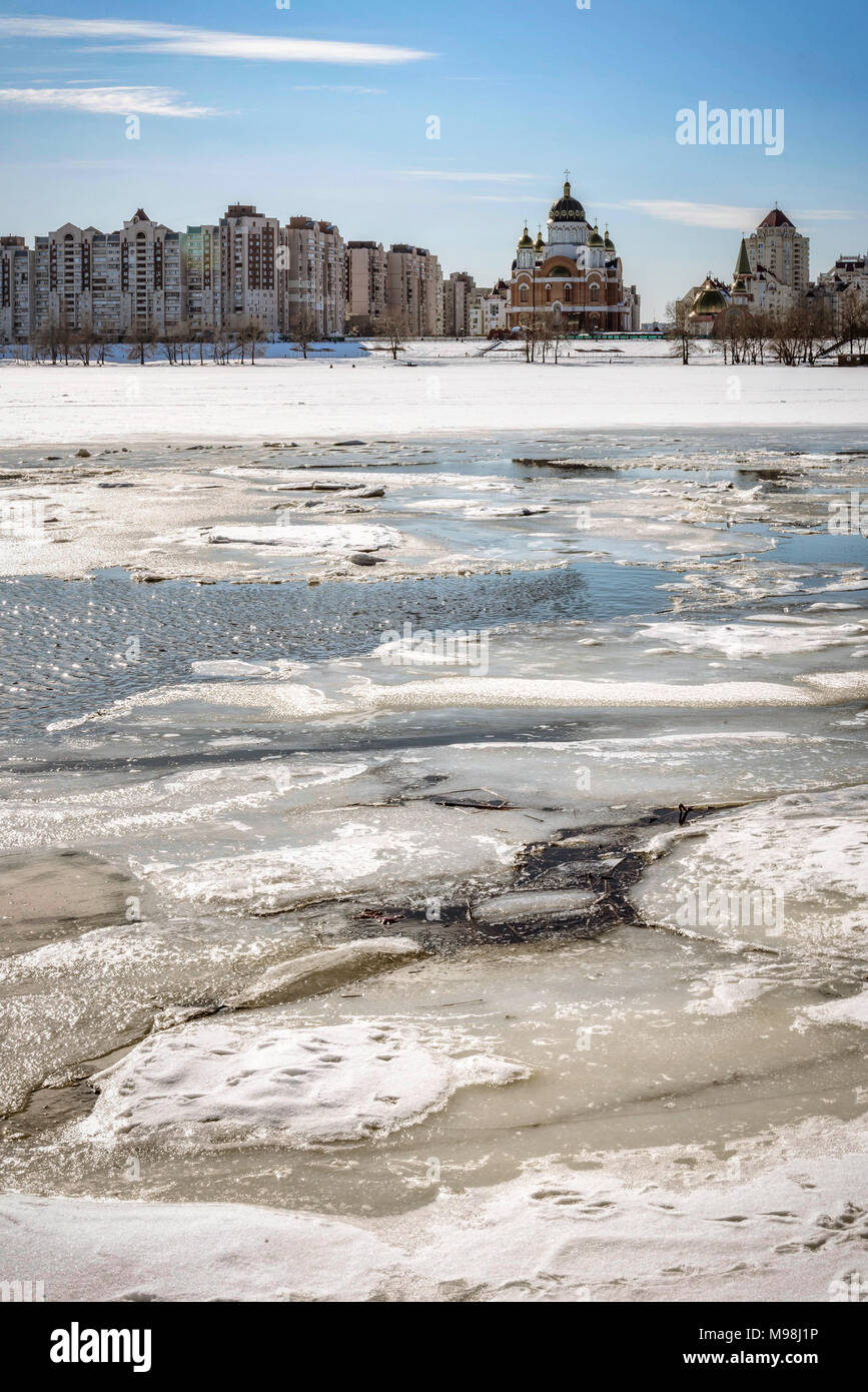 Vista di salici e pioppi vicino al congelato sul fiume Dnieper a Kiev durante l'inverno. Edifici alti e la Cattedrale di intercessione della falena Foto Stock