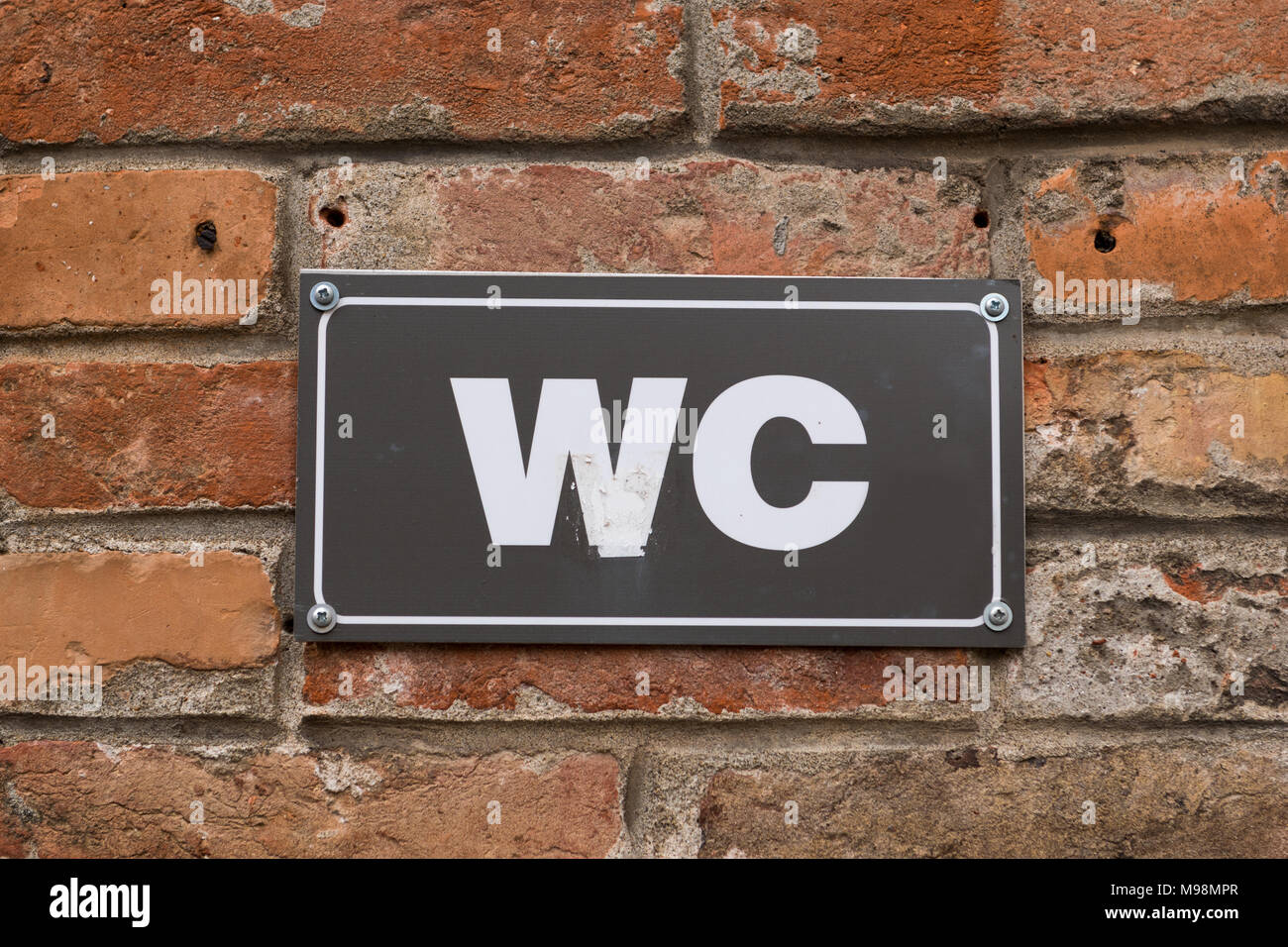 Servizi igienici WC segno sul vecchio rosso un muro di mattoni. White WC segno nero sulla piastra metallica. Segno esterno. Foto Stock