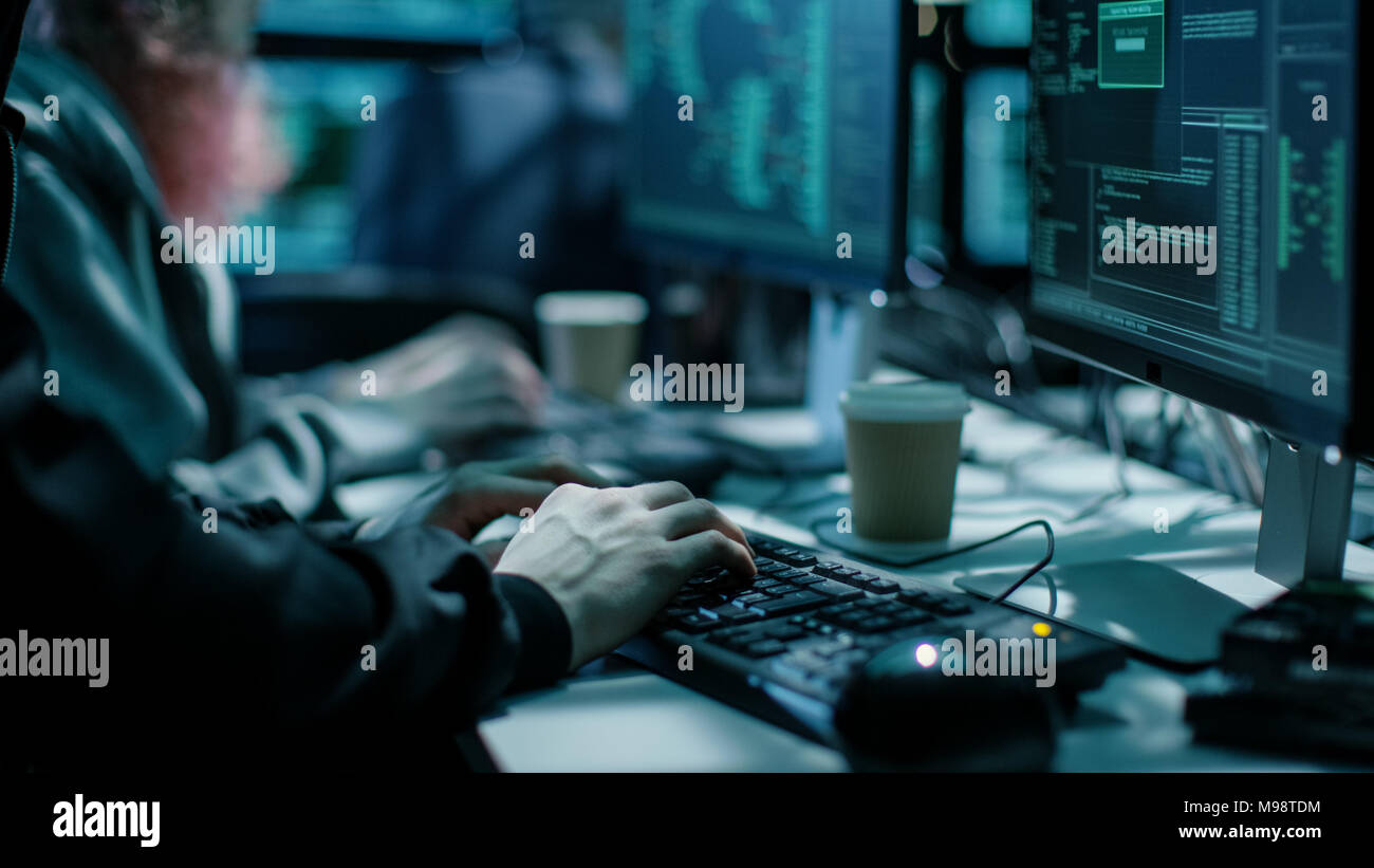 Close-up shot di Hacker utilizzando la tastiera. Vi è di tazze da caffè e monitor di computer con varie informazioni. Foto Stock