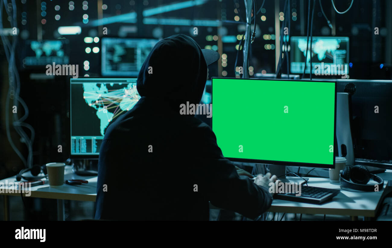 Hacker adolescenti sta lavorando con il suo computer con schermo verde mock-up Display infettare i server e infrastruttura con malware. Il suo nascondiglio è scuro. Foto Stock