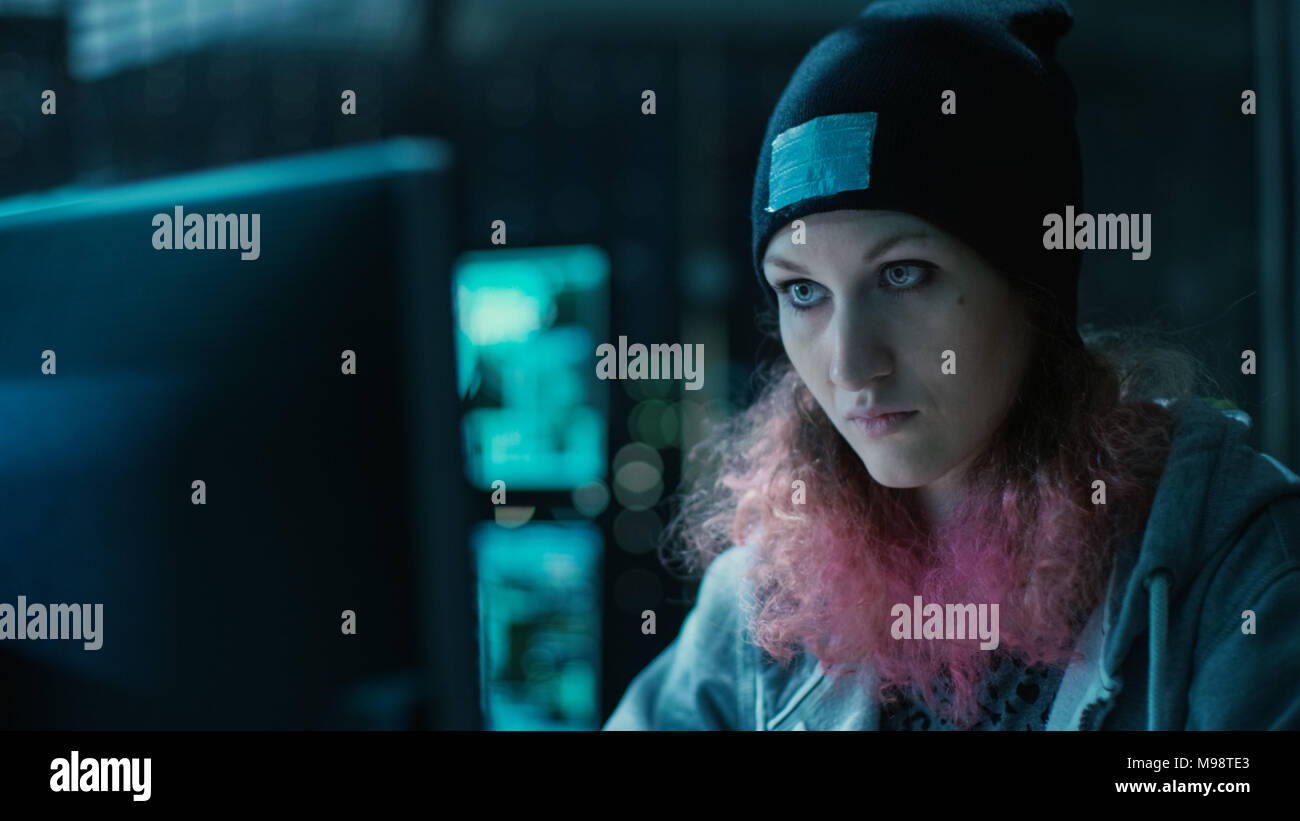 Anticonformista hacker adolescenti ragazza con i capelli rosa attacca i server aziendali con malware. La camera è scuro, Neon e ha molti Visualizza. Foto Stock