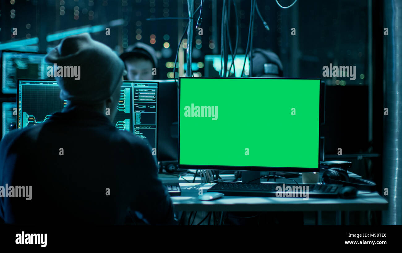 Colpo di hacker adolescenti lavora con schermo verde mock-up Display di infettare i server e infrastruttura con malware. Il suo nascondiglio è scuro, illuminati al neon. Foto Stock