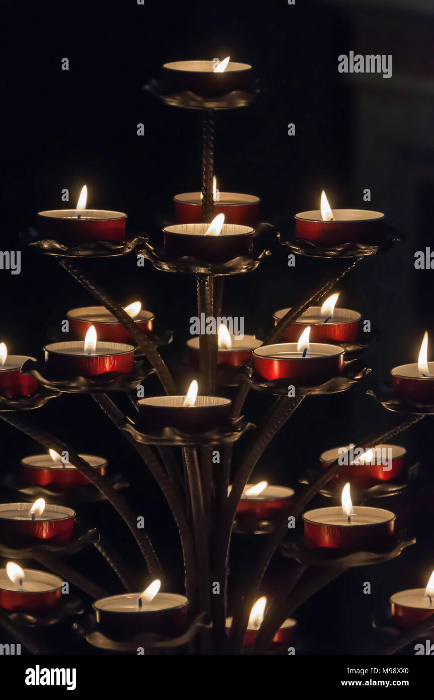 Piramide di candele votive in rosso di contenitori di metallo in una chiesa oscura Foto Stock