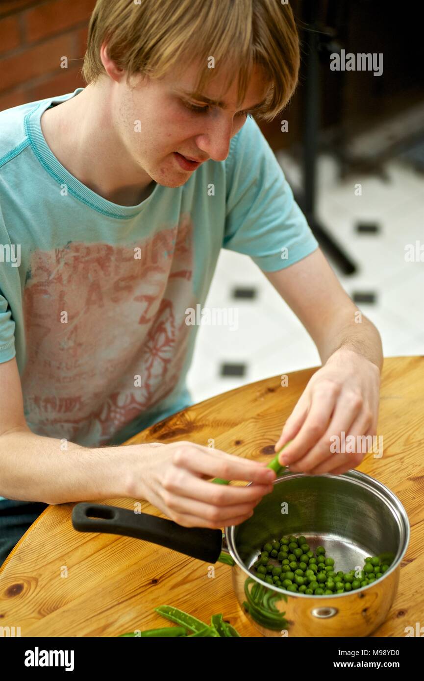 Giovane uomo piselli da sgranare in un tegame in una cucina di paese Foto Stock