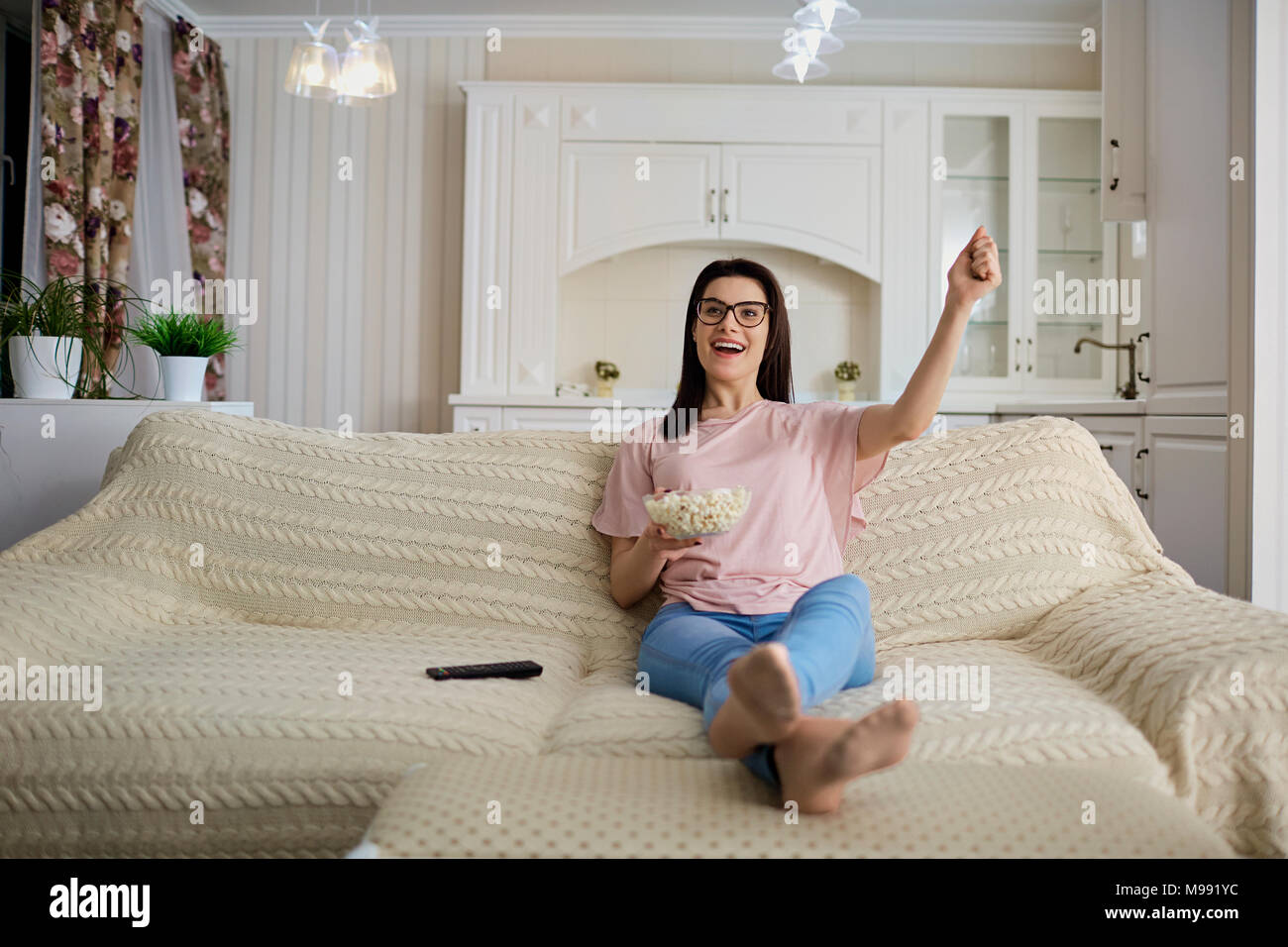 Una bruna ragazza con gli occhiali con popcorn guardando la TV seduto sul divano in camera. Foto Stock