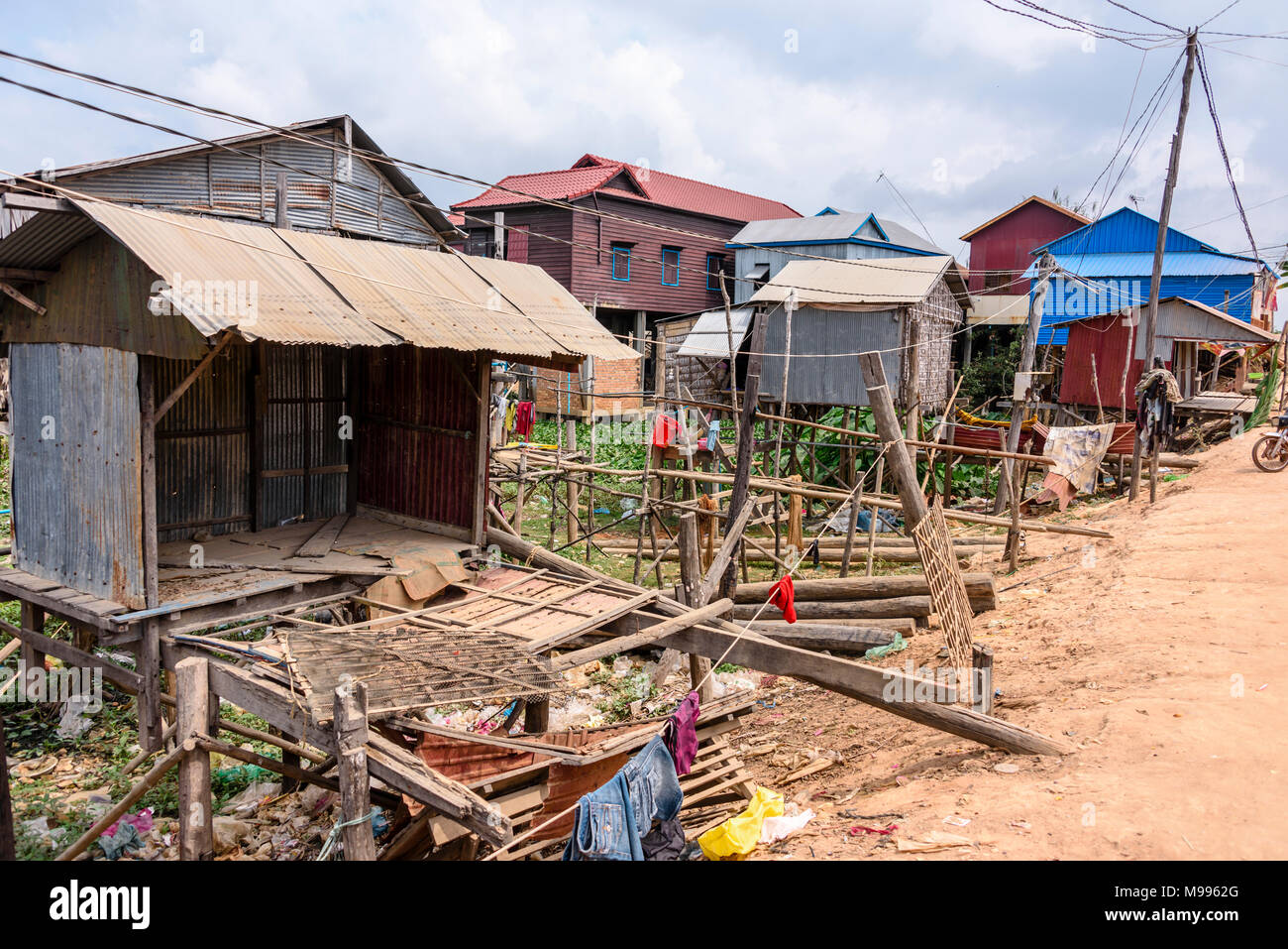 Case fatte dal ferro corrugato su palafitte di legno in un povero villaggio rurale con una pista sterrata strada in Cambogia. Foto Stock