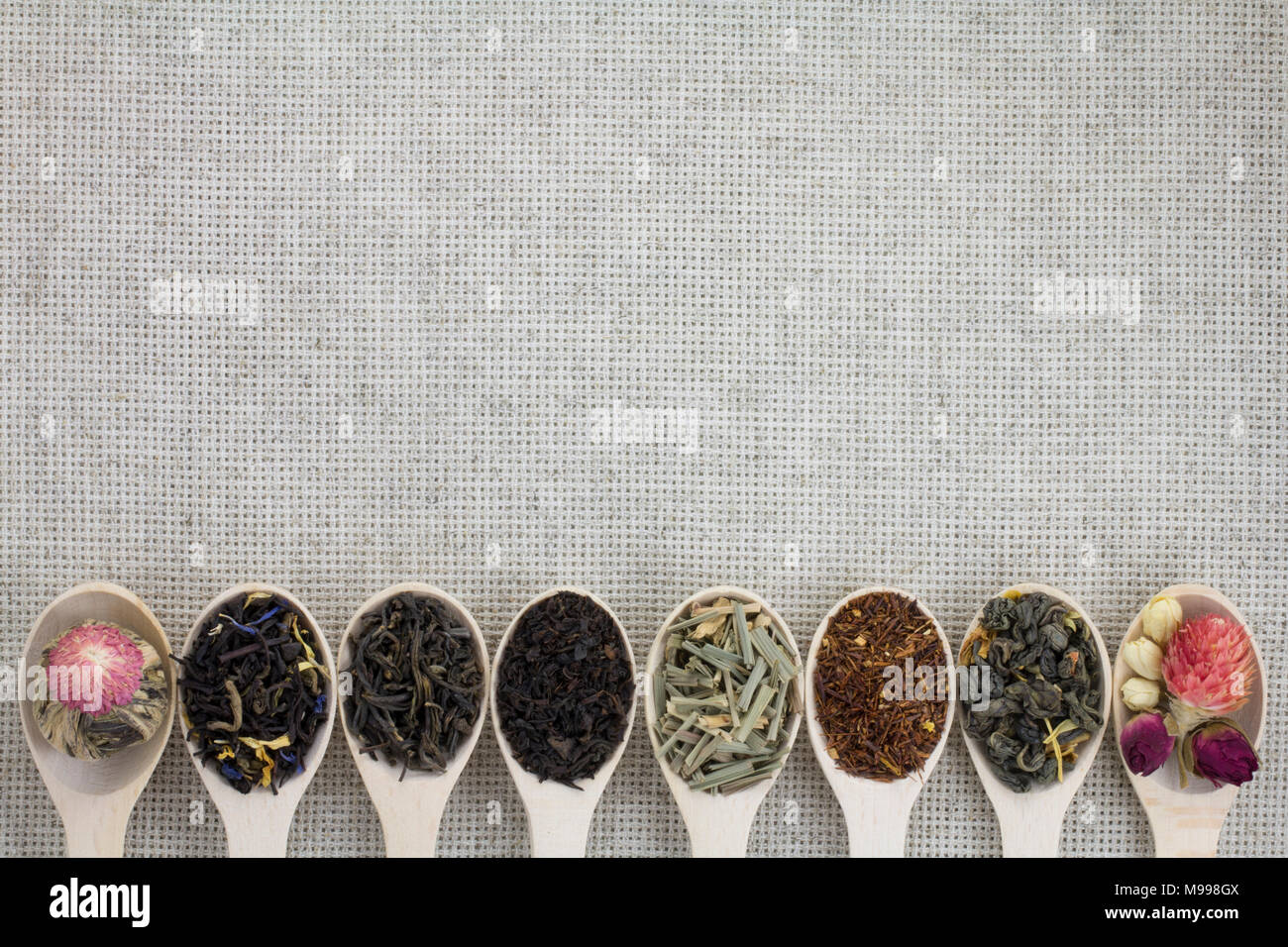 Assortimento di tipi diversi di tè in un cucchiaio di legno su uno sfondo di colore grigio tessuto naturale Foto Stock