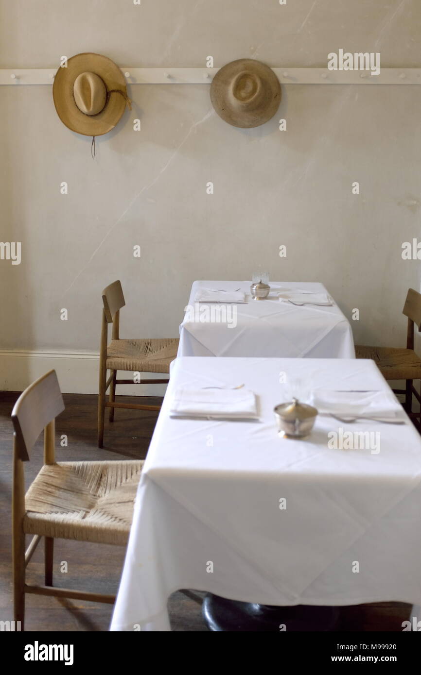 Semplice bianco tovaglia sala da pranzo con due tavoli con sedie rustiche e due cappelli sulla parete. Foto Stock