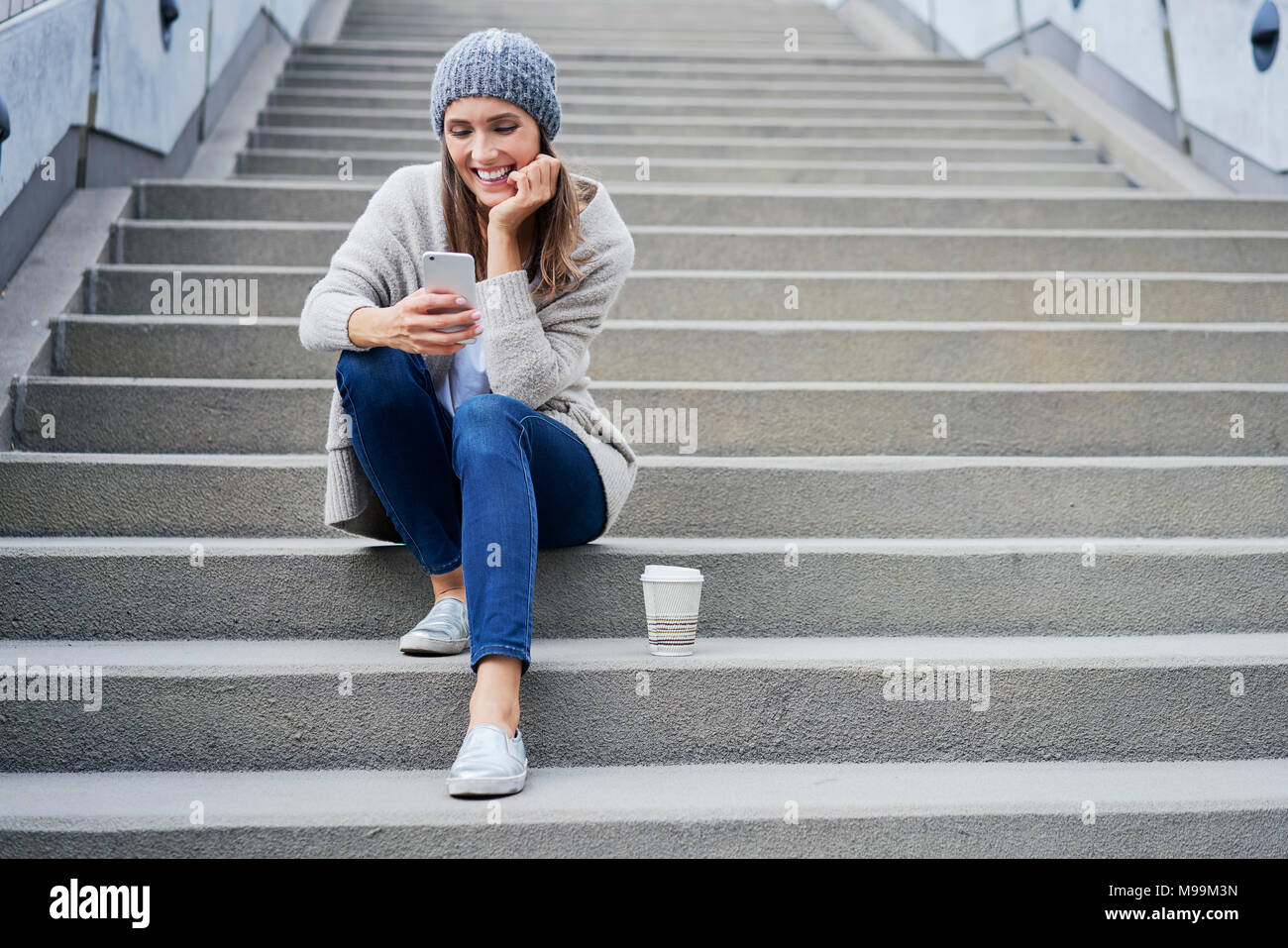 Donna felice con caffè per andare seduti sulle scale guardando al telefono cellulare Foto Stock