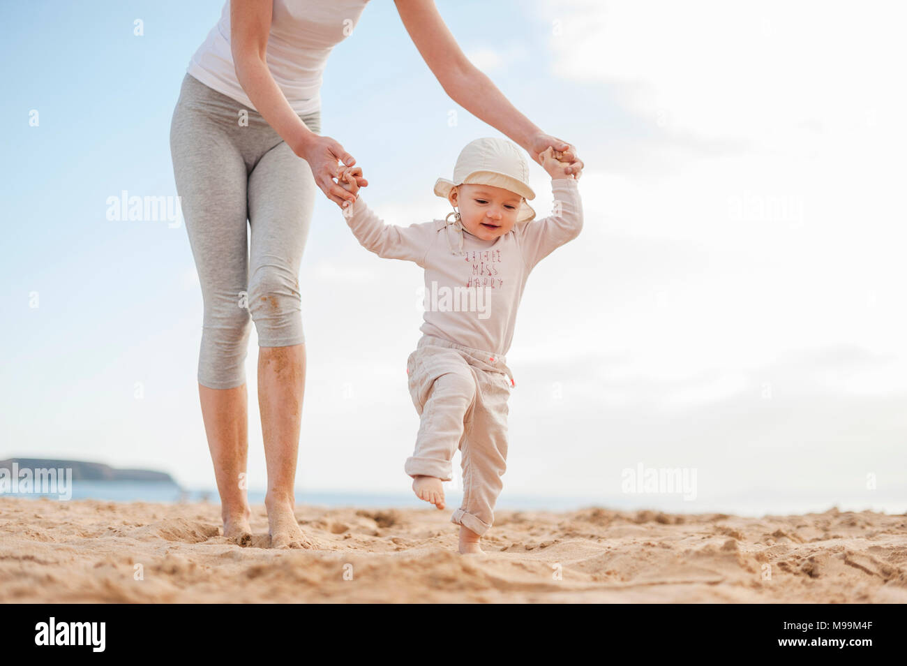 Madre aiutare piccola figlia di camminare sulla spiaggia Foto Stock