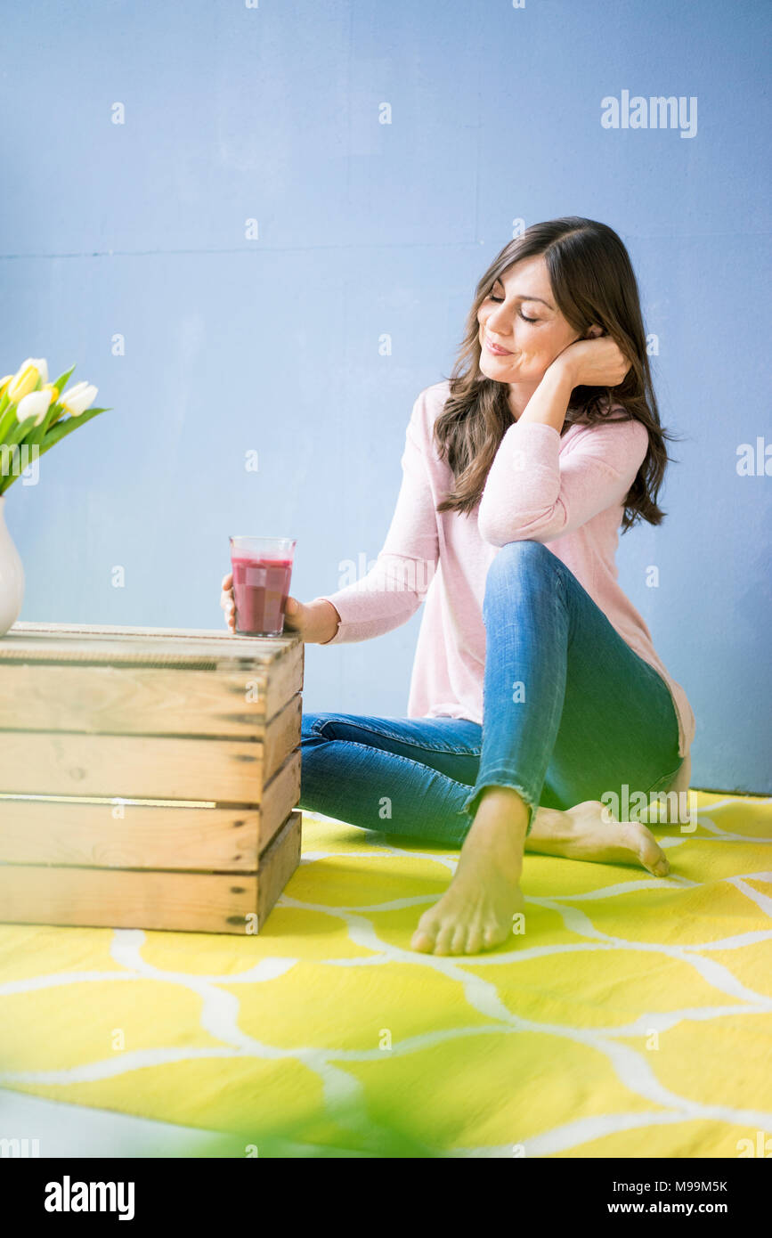 Donna sorridente seduto sul pavimento afferrando un bicchiere di succo di frutta Foto Stock