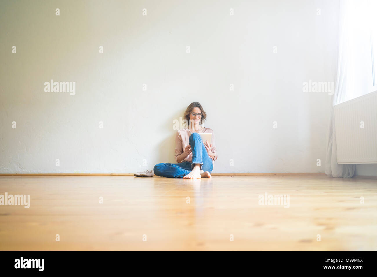 Sorridente donna matura seduta sul pavimento nella stanza vuota utilizzando tablet Foto Stock