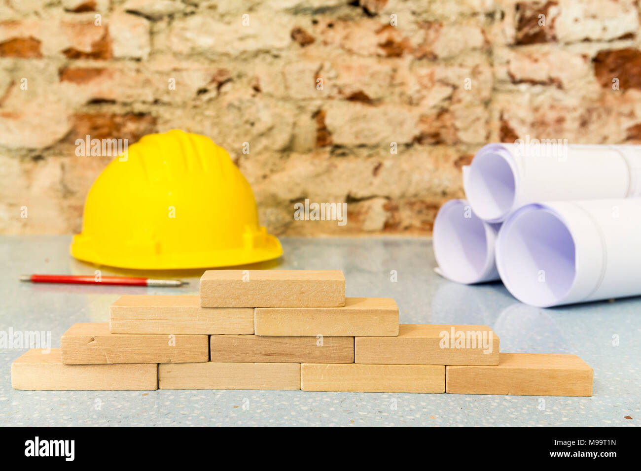 Piccoli blocchi di legno, casco e disegni di progetto su un muro di mattoni sfondo Foto Stock