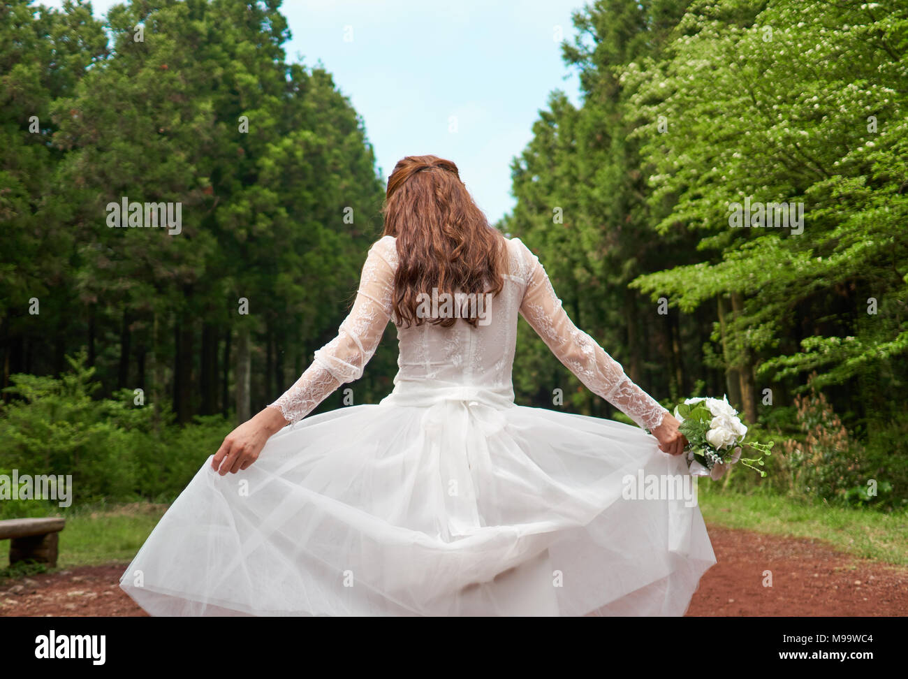 La donna in bianco allacciato abito sposa bouquet di contenimento in una foresta Foto Stock