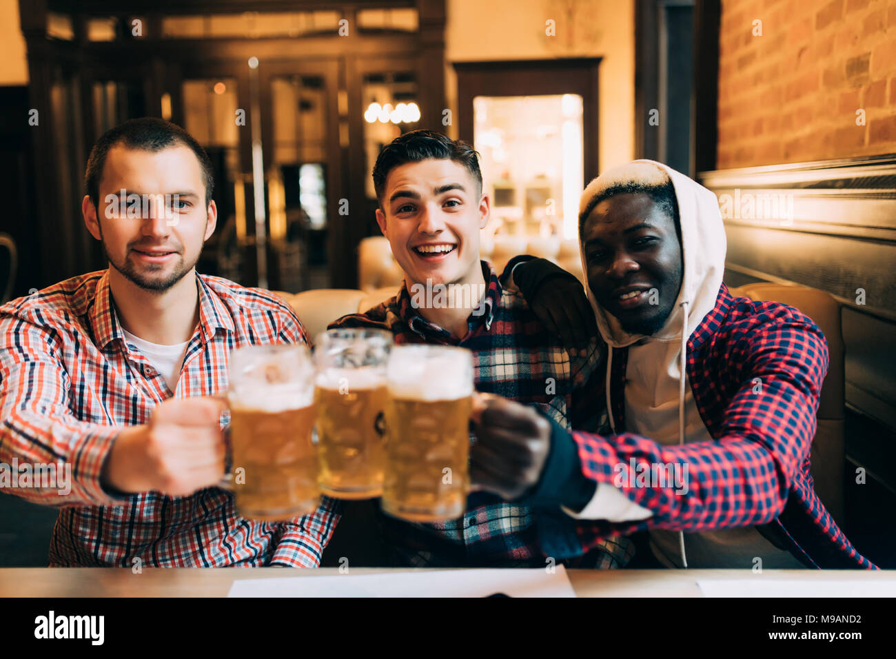 Happy amici maschi a bere birra e tintinnanti bicchieri al bar o pub Foto Stock