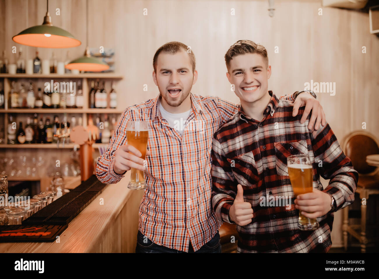 Due prestanti giovani in abbigliamento casual azienda bicchieri con birra e  guardando lontano mentre in piedi al bancone del bar Foto stock - Alamy