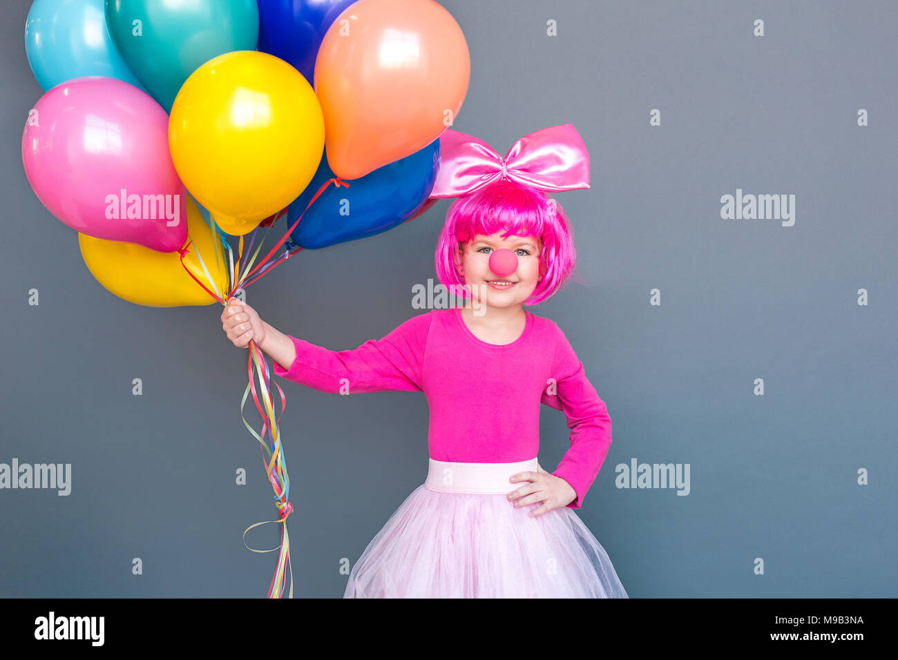 Bello piccolo clown tenendo un sacco di palloncini. Festeggiare il compleanno. Studio shot, isolata su uno sfondo grigio Foto Stock