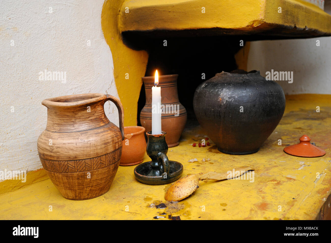 Tradizionale ucraino creta, vaso, cucchiaio di legno e candela bruciante posto vicino vecchio forno rustico. Kiev, Ucraina Foto Stock