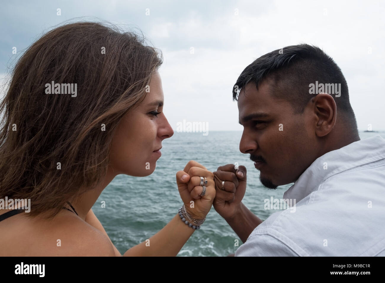 Coppia giovane seduto sulla Ocean Shore. Si stringono le mani in un pugno. Promettono di essere forte e vera per ogni altro. Foto Stock