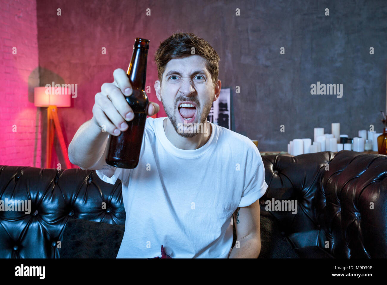 Sostenitore del giovane uomo guardando la partita di calcio in tv seduti a casa lettino con birra e patatine nella sollecitazione sconsolato e deluso per la mancata sho Foto Stock