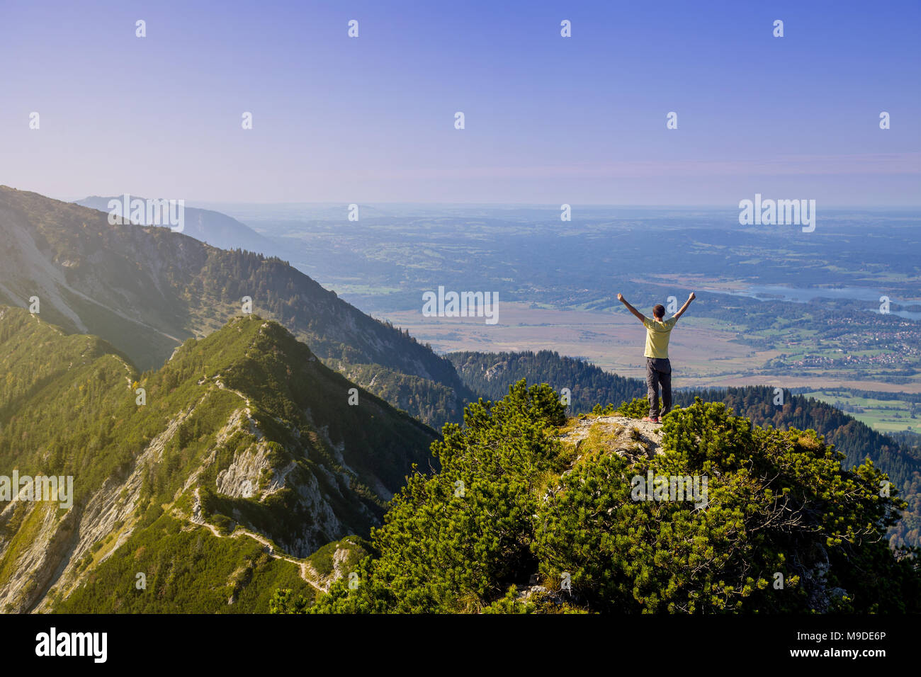 Giovane uomo di raggiungere la parte superiore del Herzogstand con bellissima vista verso i contrafforti alpini in Baviera, Germania Foto Stock