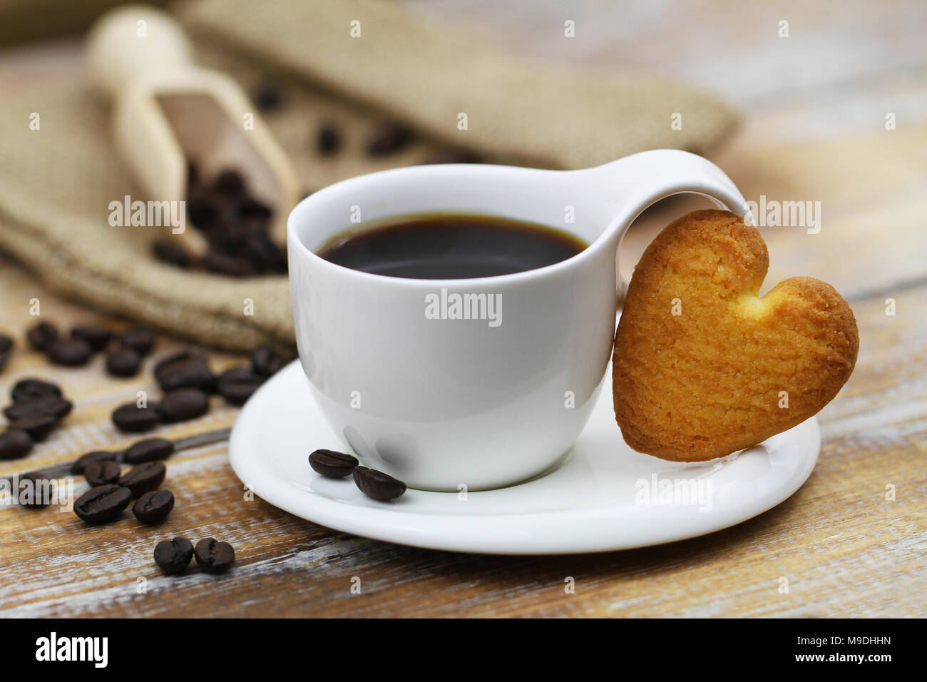 A forma di cuore ad cookie appoggiata contro la tazza di caffè rustico sulla superficie di legno Foto Stock