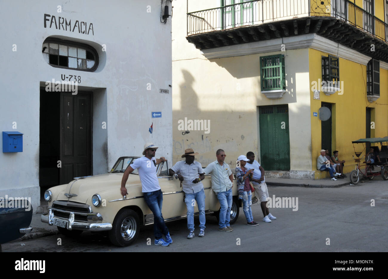 Un gruppo di persone appoggiarsi contro un classico auto parcheggiate al di fuori di una farmacia su Calle Oficios (street) nella Vecchia Havana, Cuba. Foto Stock