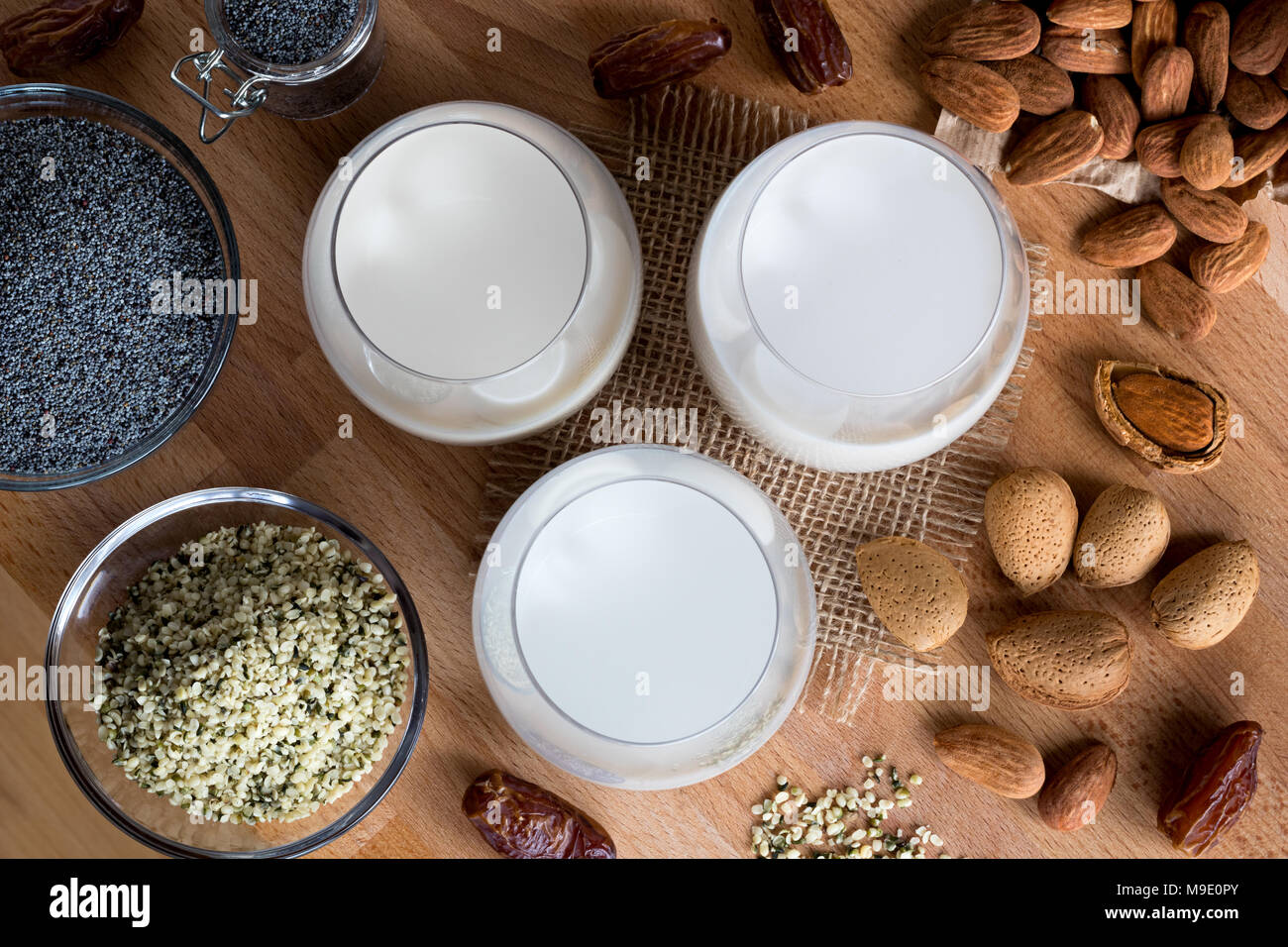 Vista superiore di tre bicchieri di vegano latte vegetale - latte di mandorla, semi di papavero e latte di semi di canapa, di latte con sgusciati e mandorle senza guscio, semi di papavero, canapa Foto Stock