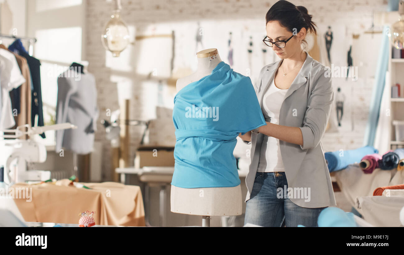 Bella donna moda, designer, lavorando con manichini di sartoria, cercando su vari ornamenti e tessuti. Il suo studio è luminosa e soleggiata. Foto Stock