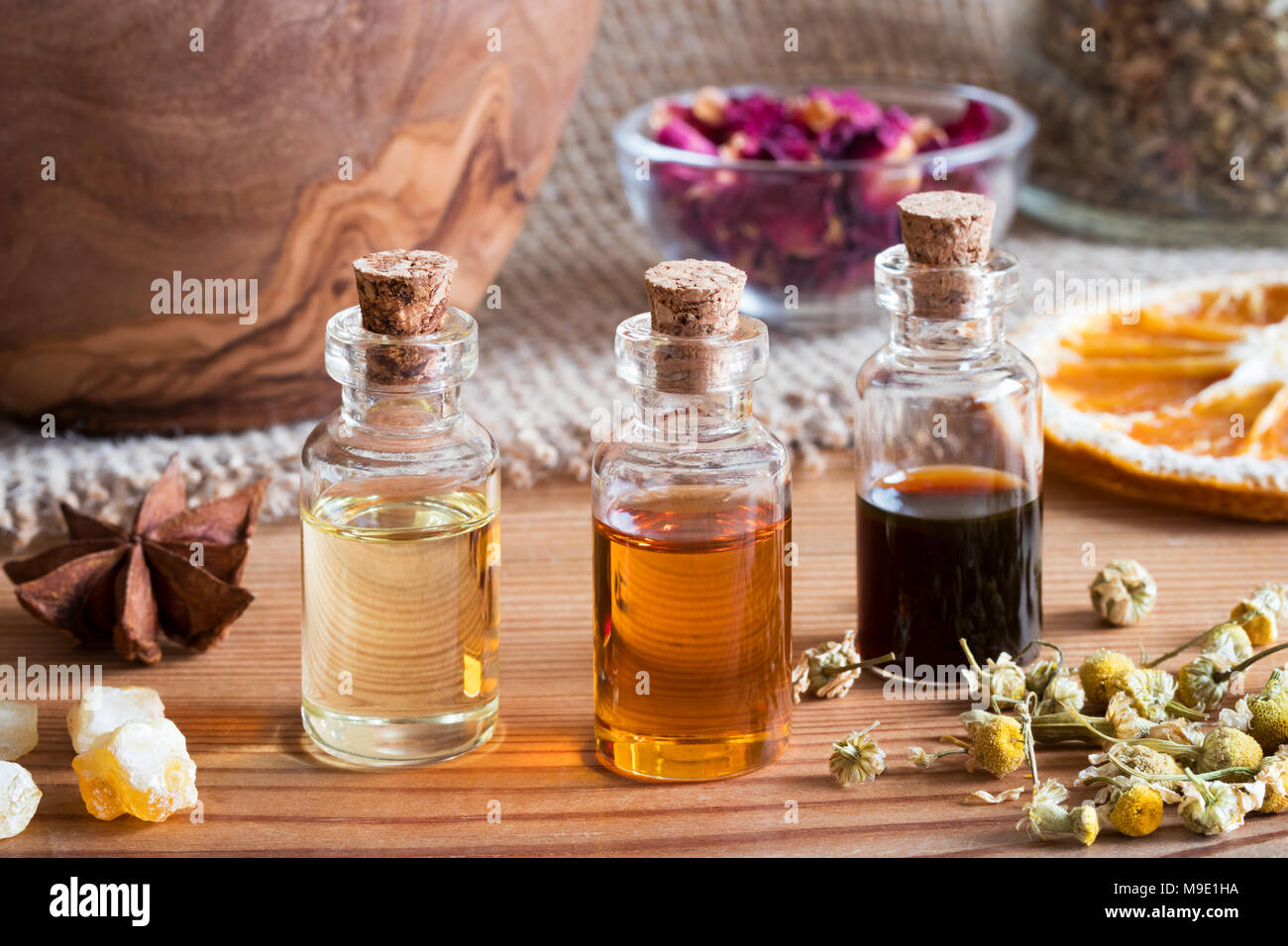 Bottiglie di olio essenziale con anice stellato, incenso, essiccati i fiori di camomilla essiccata e fettine di arancia Foto Stock