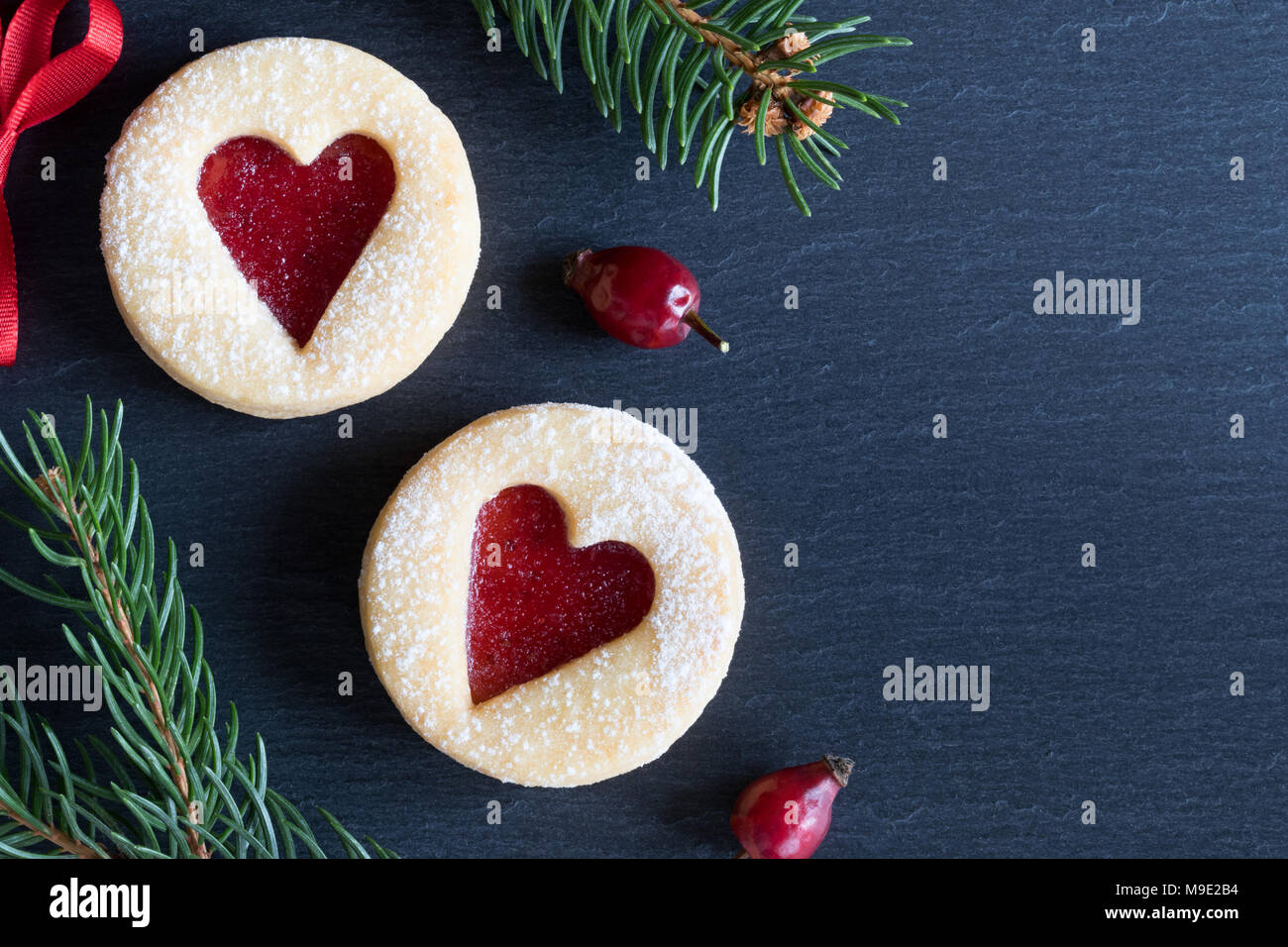 Sfondo di natale con due Linzer biscotti di Natale con cuore forme, essiccato, rosa canina e rami di abete rosso Foto Stock