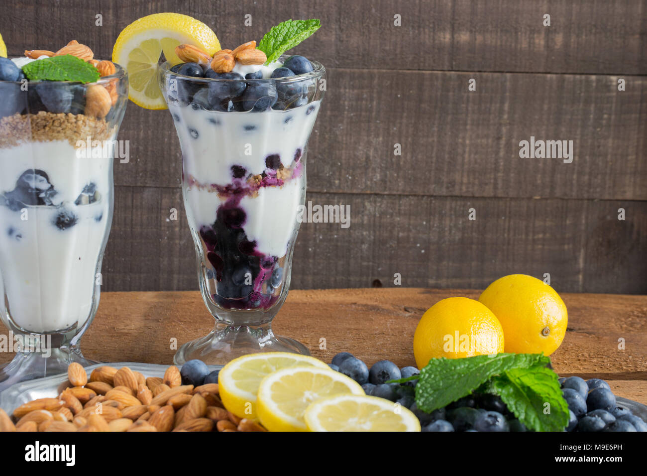 Trattare sano - lo yogurt greco in un dessert fantasia vetro - parfait con mirtilli freschi, mandorle tritate, granola, una spremuta di limone e rametto di menta Foto Stock