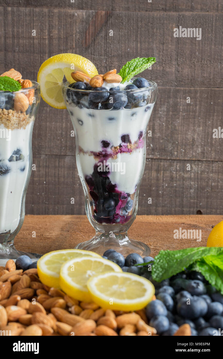 Trattare sano - lo yogurt greco in un dessert fantasia vetro - parfait con mirtilli freschi, mandorle tritate, granola, una spremuta di limone e rametto di menta Foto Stock