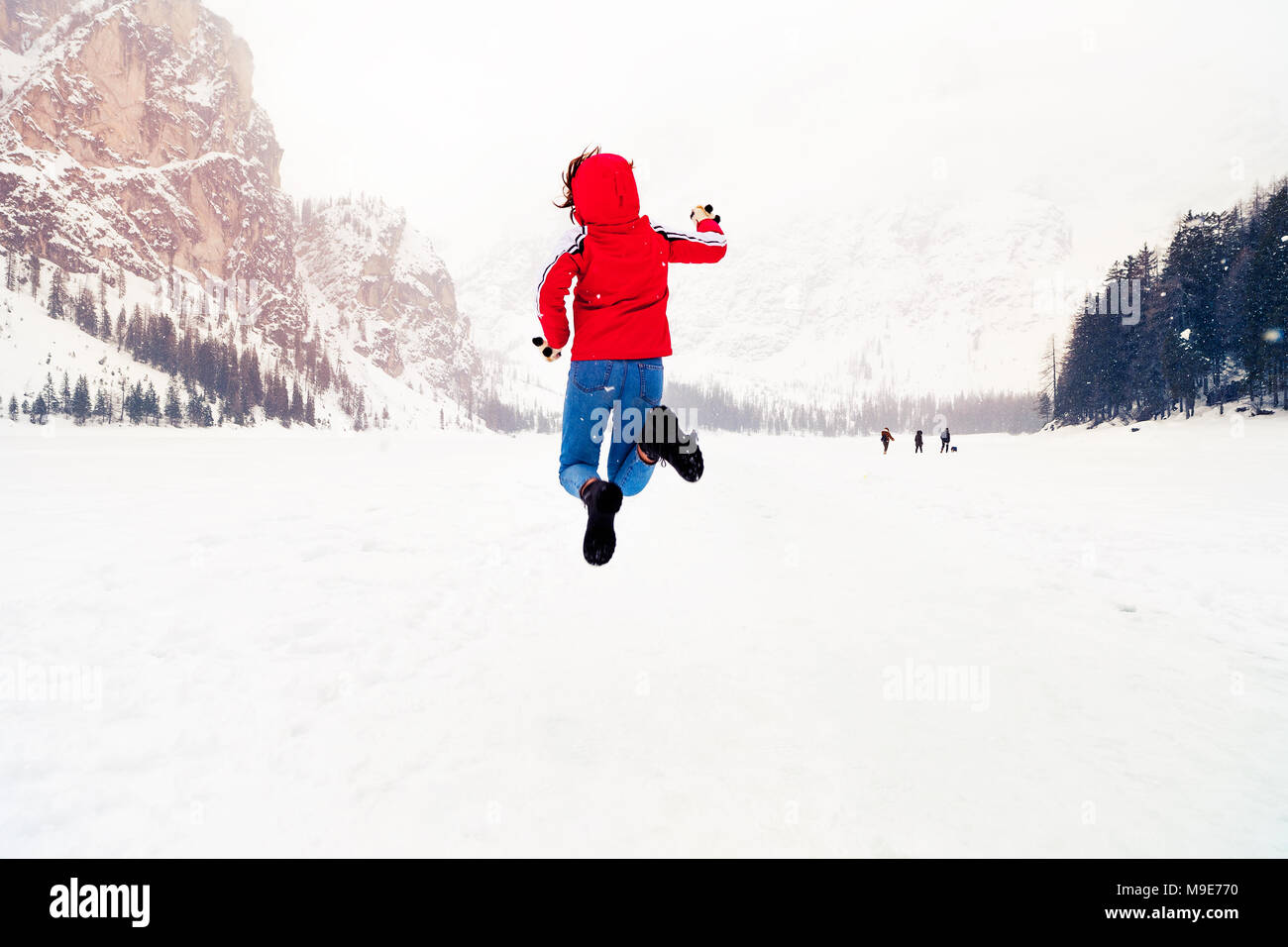 A tutta lunghezza shot di soggetti di razza caucasica Allegra donna far levitare su lago ghiacciato di Braies in background, esprimendo felicità e divertimento Foto Stock