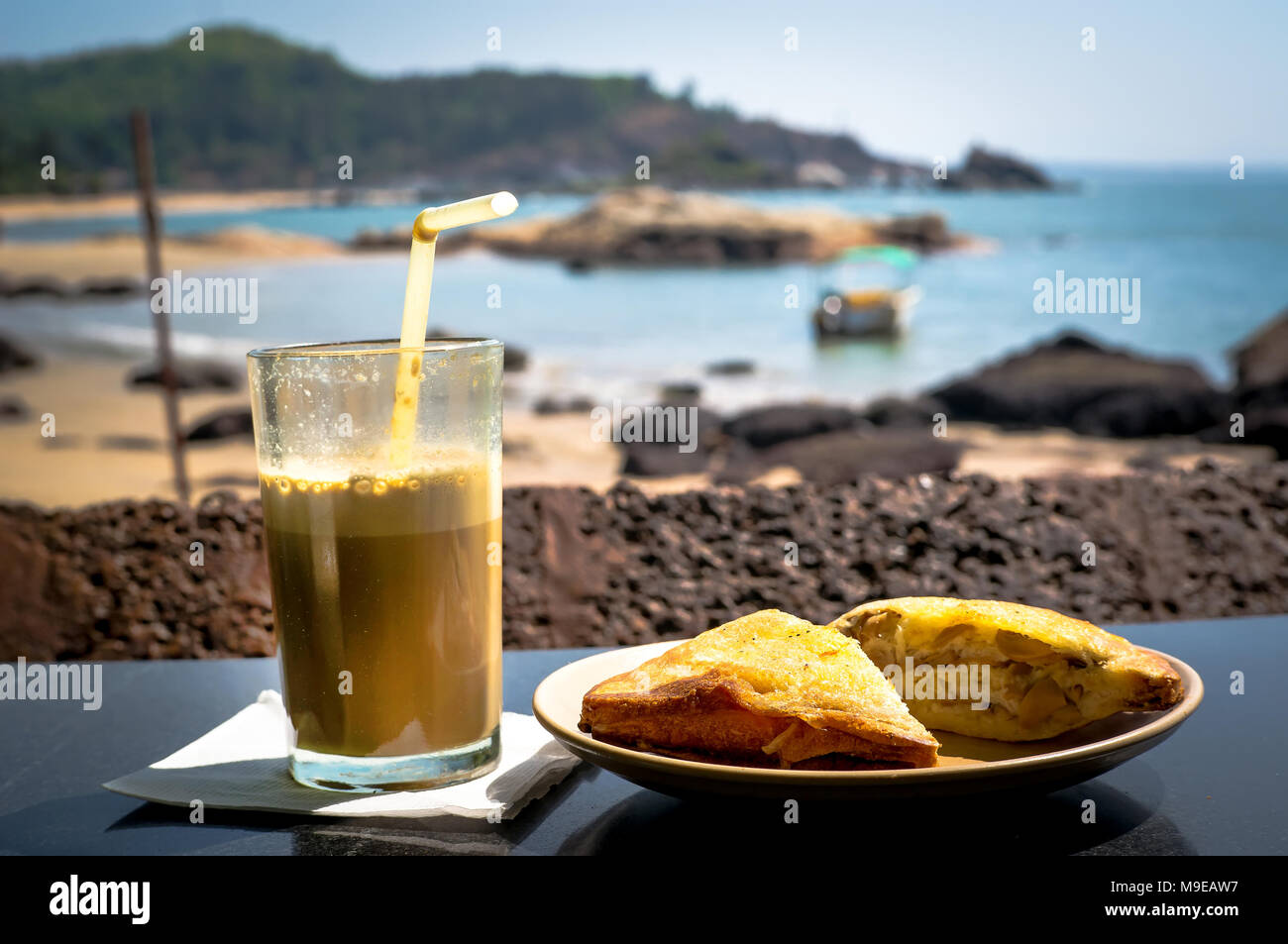 La prima colazione sulla spiaggia. Un panino e un cocktail di caffè sul tavolo nel ristorante sullo sfondo del mare su una calda giornata di sole. Foto Stock