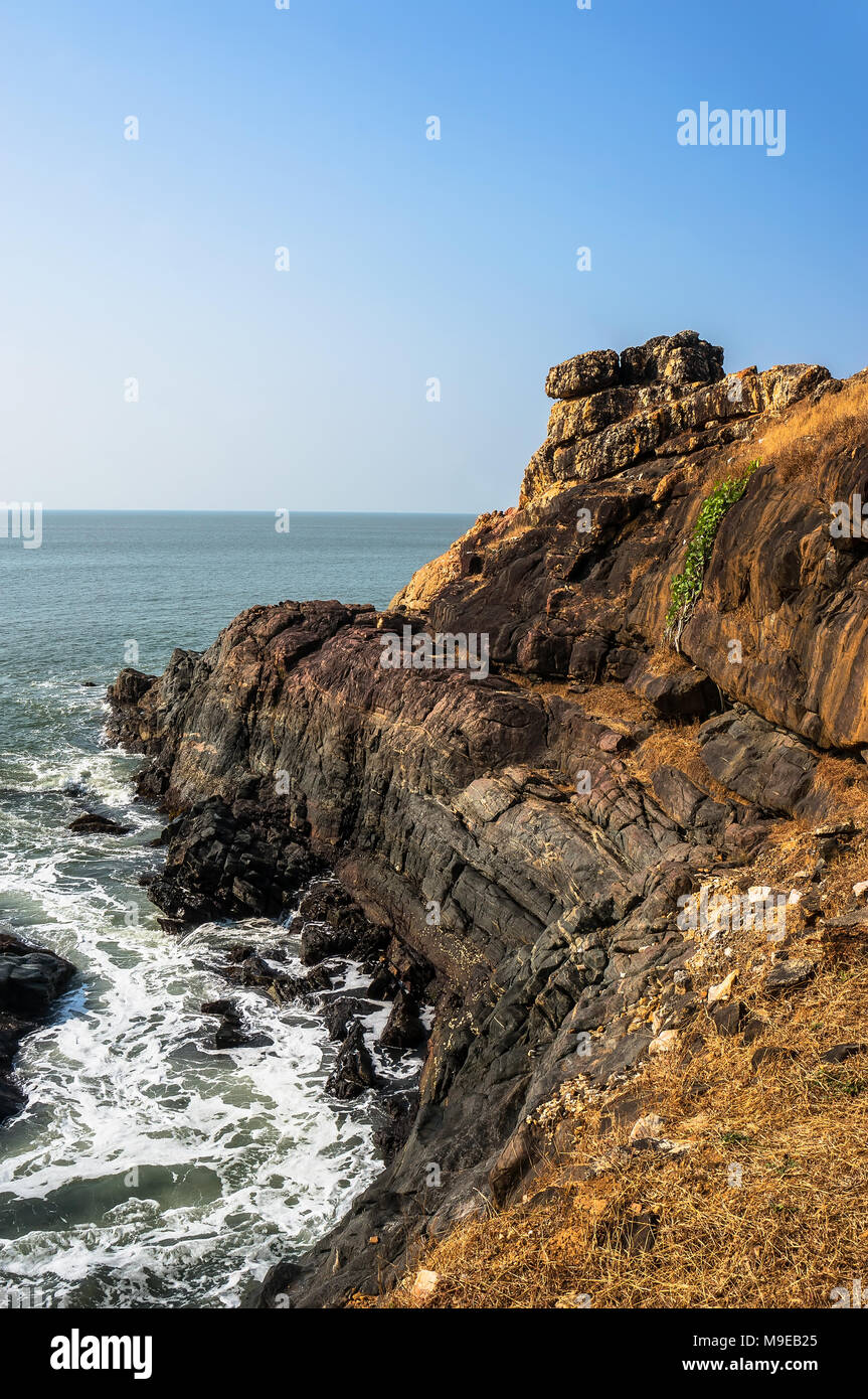 La ripida costa rocciosa con il blu del mare e le onde che si infrangono sulle rocce. Gokarna India Foto Stock
