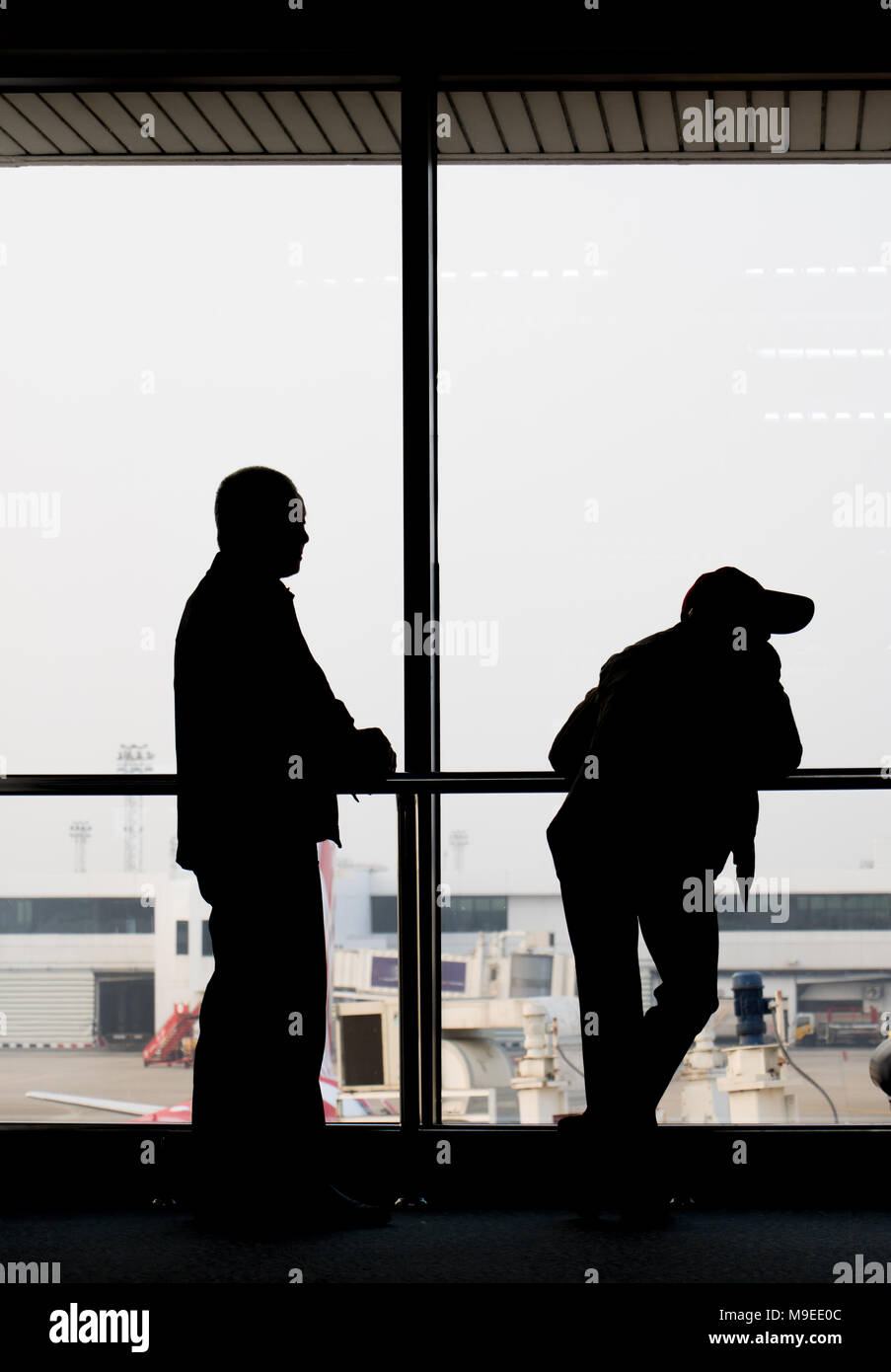 Contorni neri di passeggeri contro la finestra nell'aeroporto lobby. I passeggeri sono in attesa per il piano nel terminale. Foto Stock
