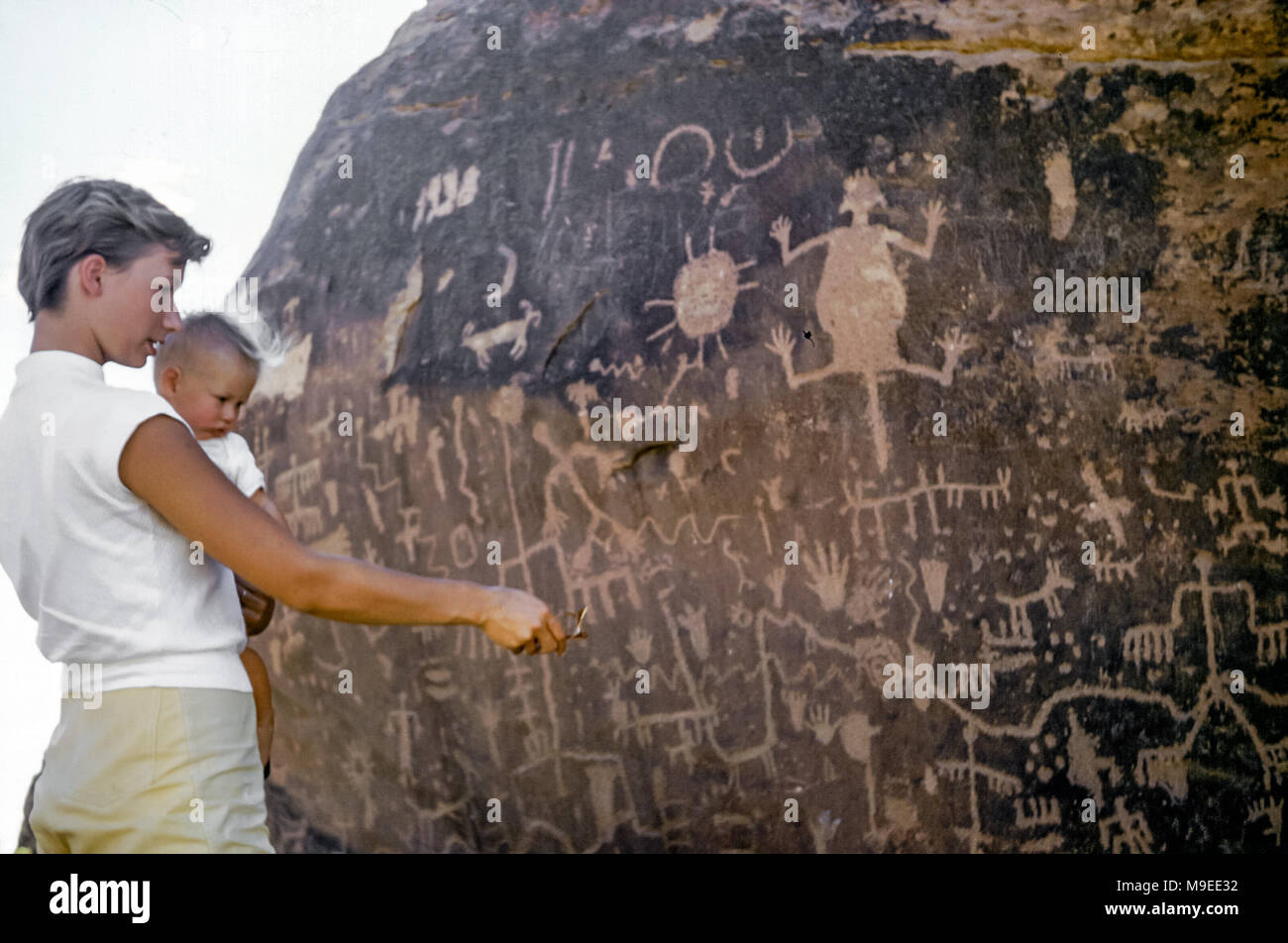 Attraente giovane donna con i capelli corti che tengono la bambina di 7 a 8 mesi che guarda i petroglifi indiani nativi americani scolpiti su un masso, giornale Rock Petroglyph, Petrifified Forest National Park, Arizona, USA negli anni '50 Foto Stock