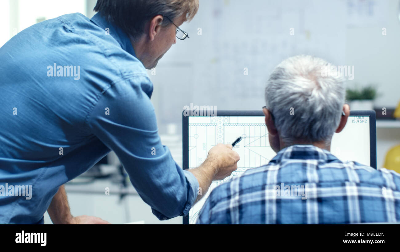 Due Senior Architectural ingegneri che lavorano con piano di costruzione su un Personal Computer. Essi attivamente discutere su vari piani e schemi. Foto Stock