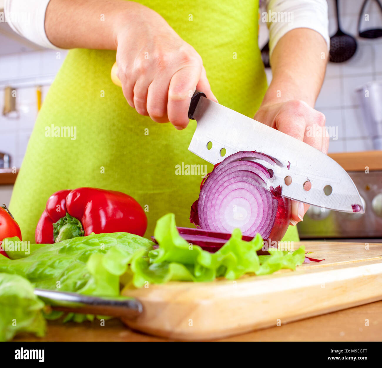 Donna con le mani in mano il taglio di Bulbo di cipolla, dietro di verdure fresche. Foto Stock