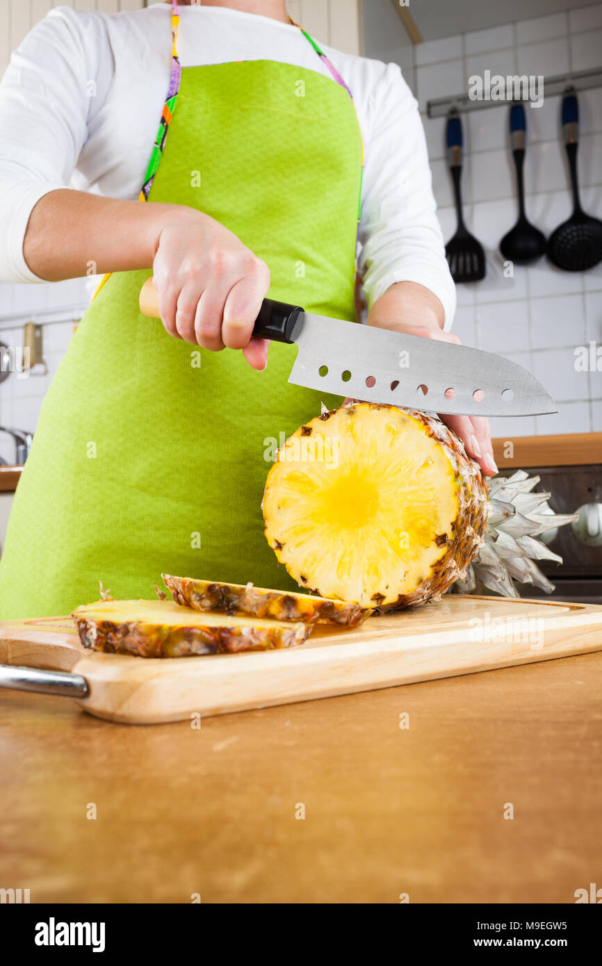 Donna con le mani in mano il taglio di ananas fresco su cucina Foto Stock