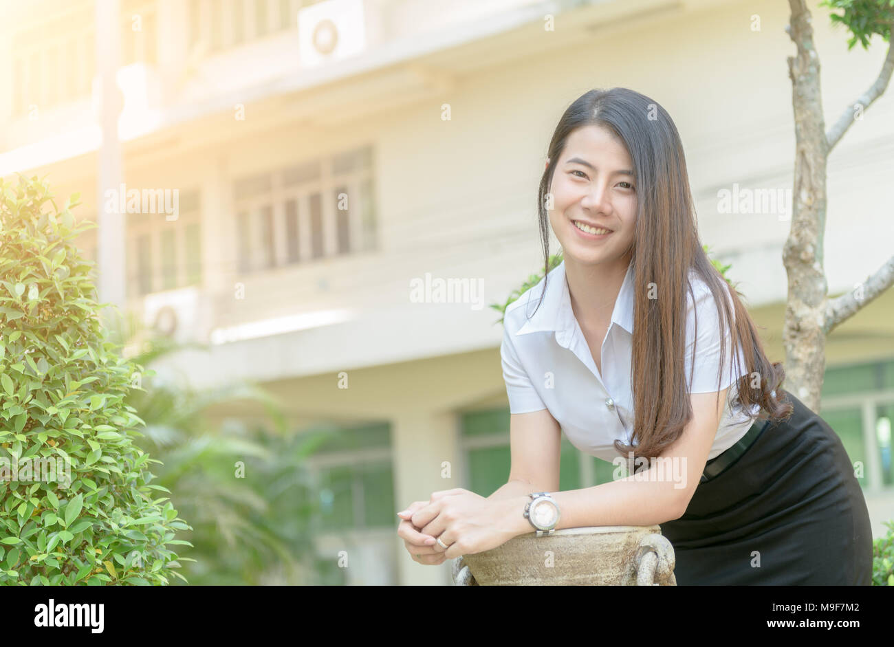 Carino giovane donna asiatica in uniforme studente sorriso e guardando la telecamera, felice e concetto di relax Foto Stock